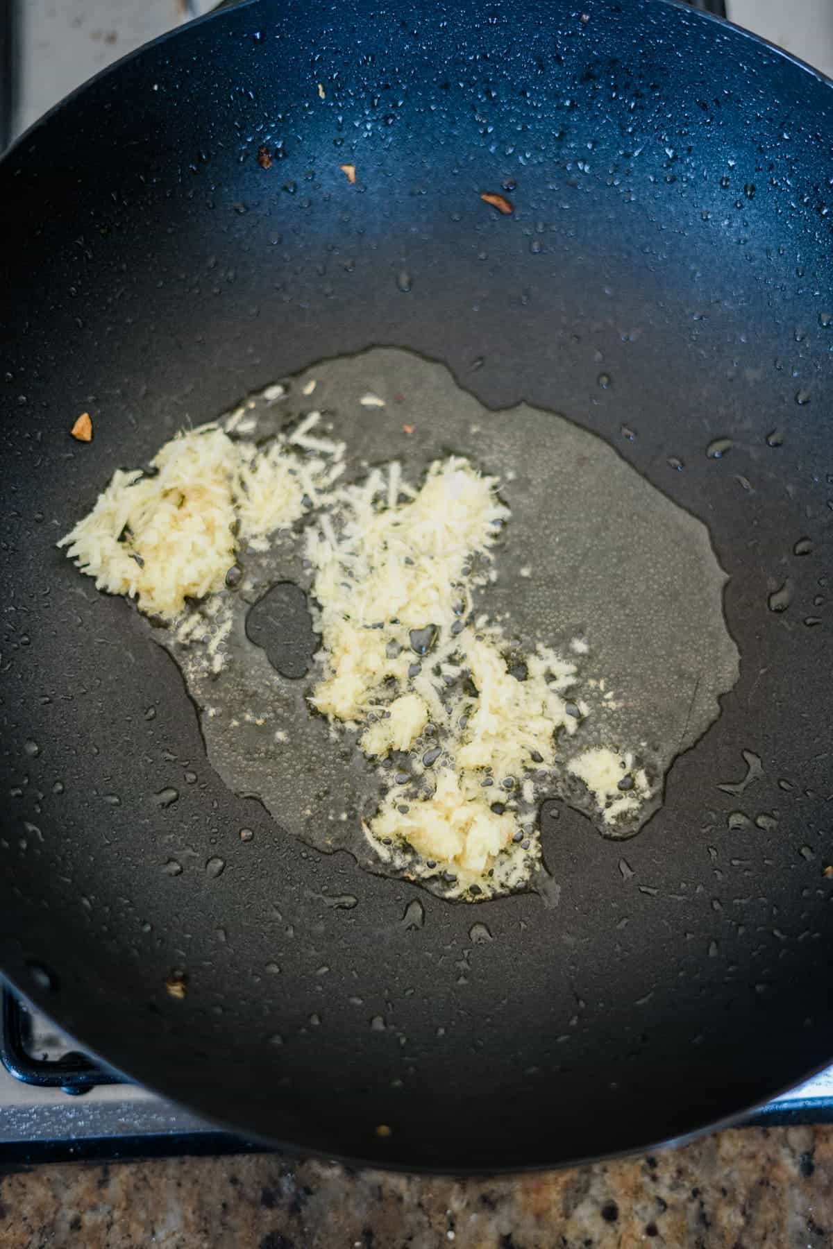 Minced garlic sautéing in oil smells divine, prepping the black frying pan for a delightful eggplant tofu recipe on the stovetop.