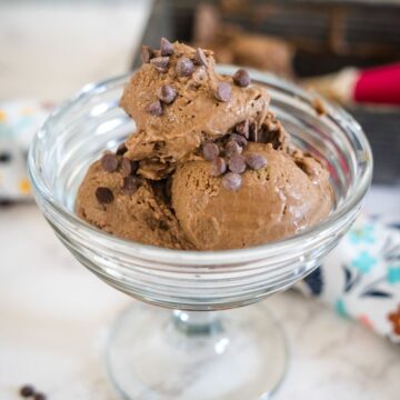 A glass dessert bowl filled with several scoops of chocolate ice cream topped with chocolate chips.