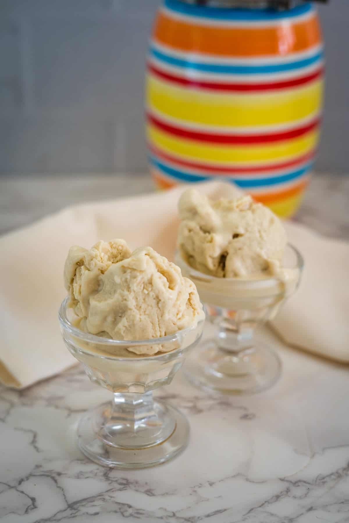 Two glass dishes with keto vanilla ice cream set on a marble surface, with a colorful striped jar in the background.