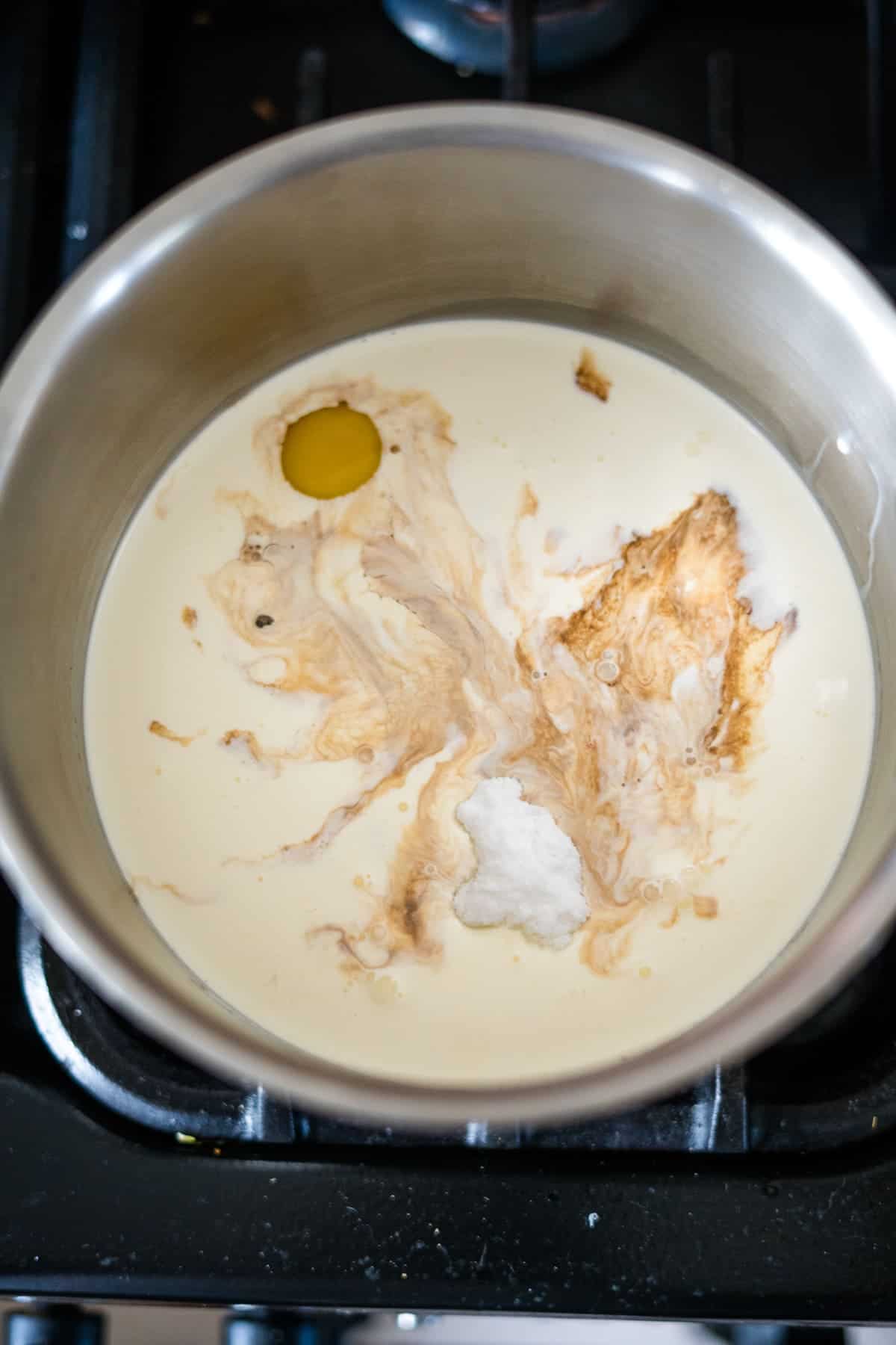 A saucepan on a stove contains cream, an egg yolk, sugar, and vanilla extract, creating the perfect base for decadent keto ice cream bars.