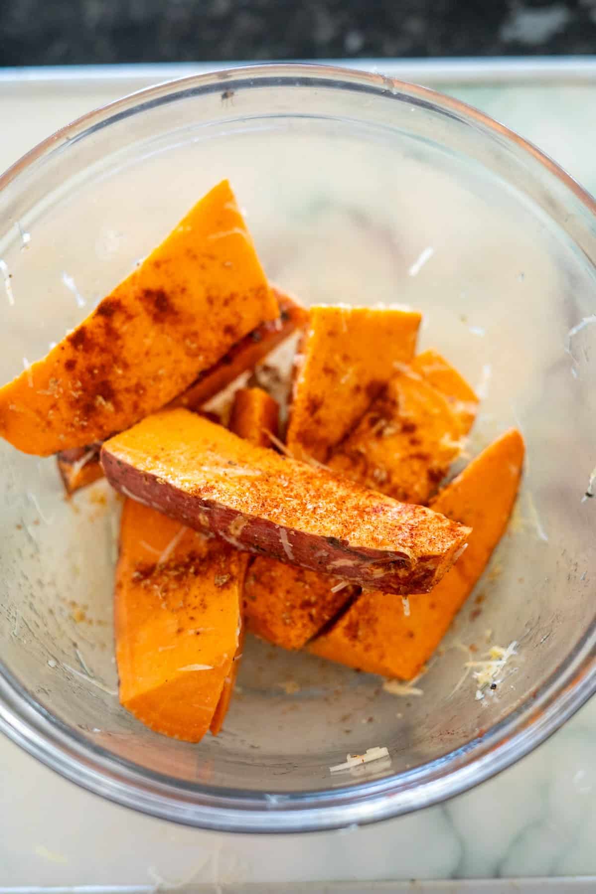 Slices of sweet potato seasoned with spices in a clear bowl.