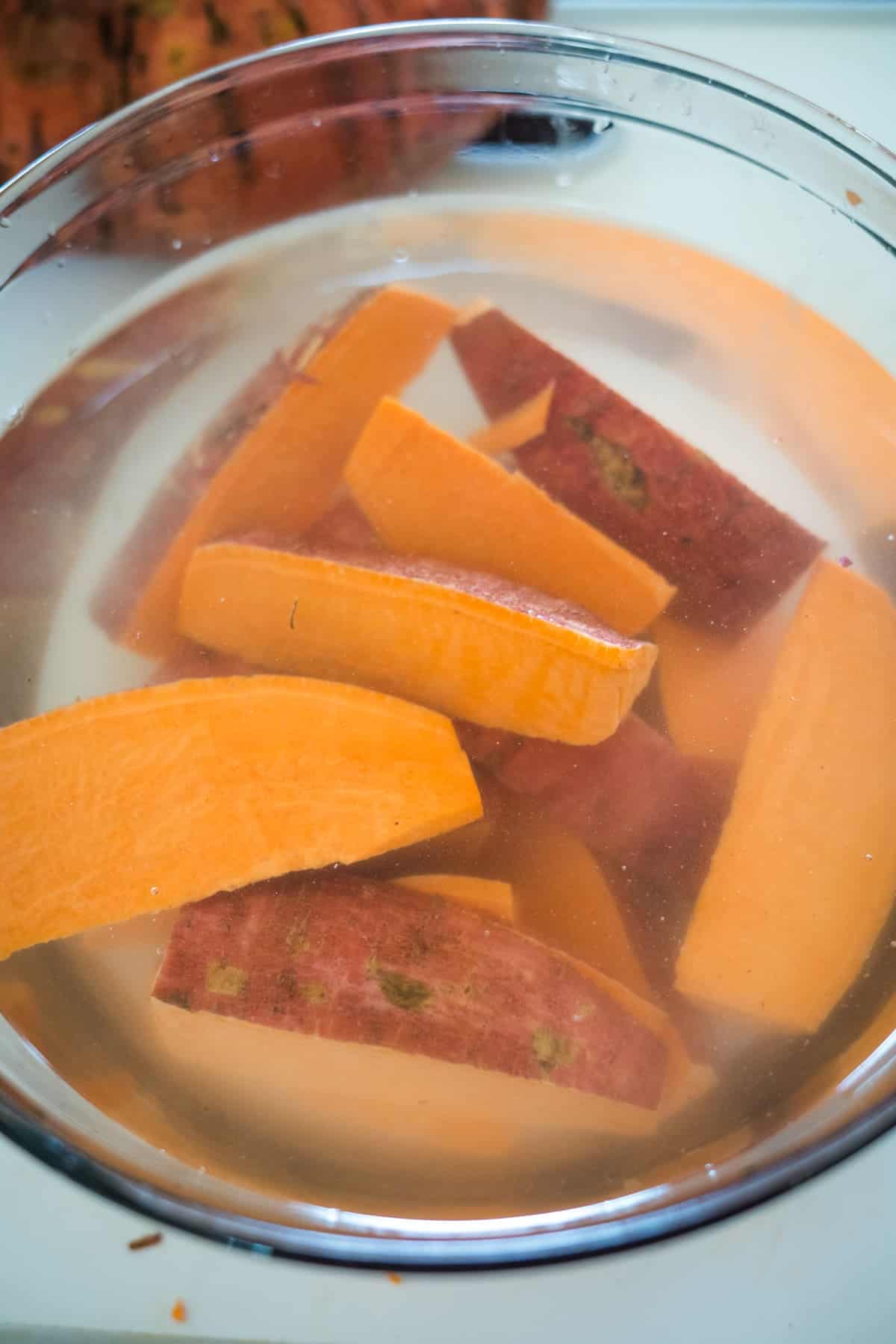 Sliced sweet potatoes soaking in a clear bowl of water.