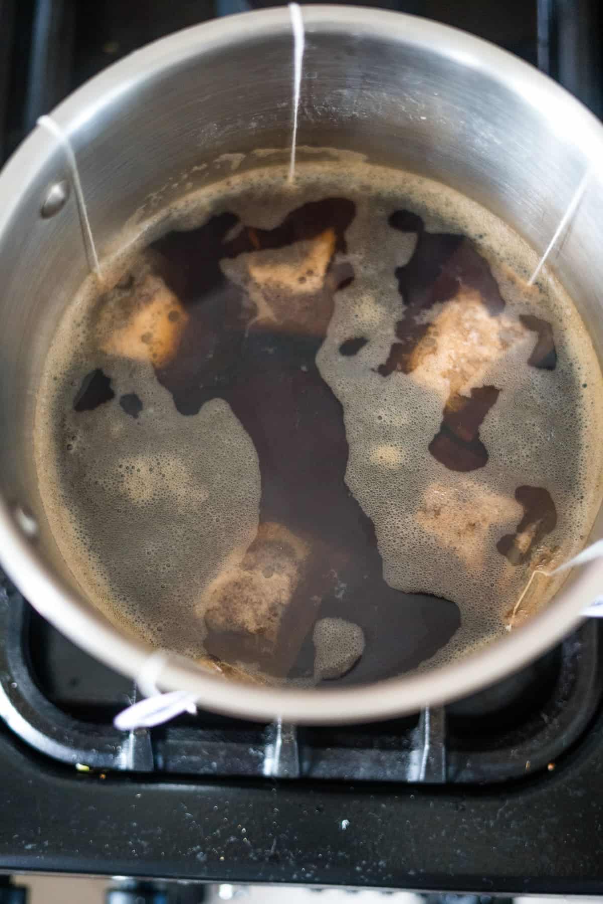 Stainless steel pot on a stove with tea bags steeping in hot water, creating a dark brown liquid.