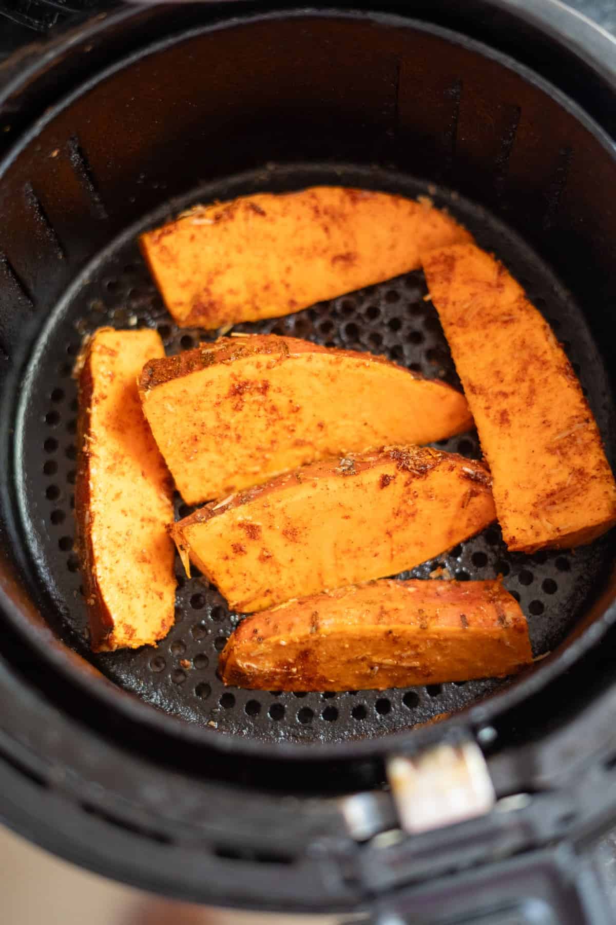 Sweet potato wedges seasoned and placed inside an air fryer basket.