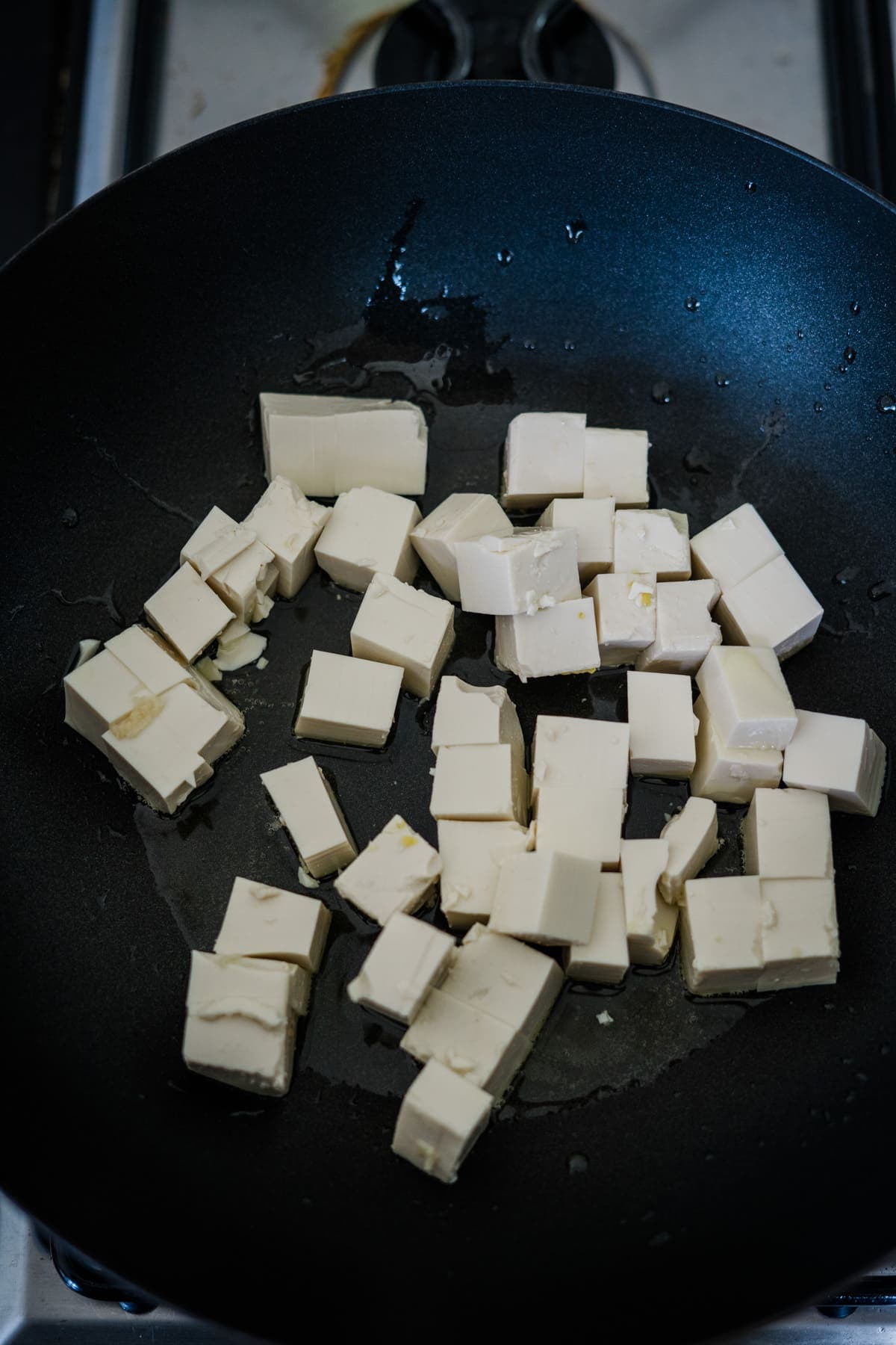 Cubes of tofu frying in a black skillet with oil, creating the perfect base for a delicious eggplant tofu recipe.