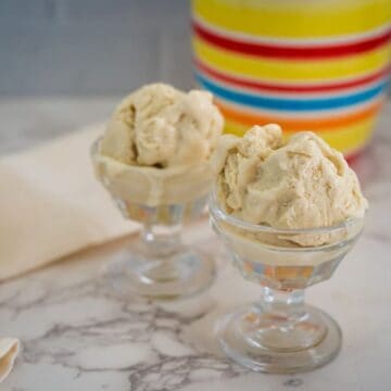 Two glass dessert bowls filled with scoops of beige-colored ice cream sit on a marble countertop, with a colorful striped container in the background.