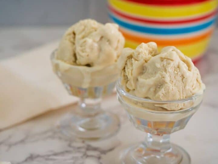 Two glass dessert bowls filled with scoops of beige-colored ice cream sit on a marble countertop, with a colorful striped container in the background.