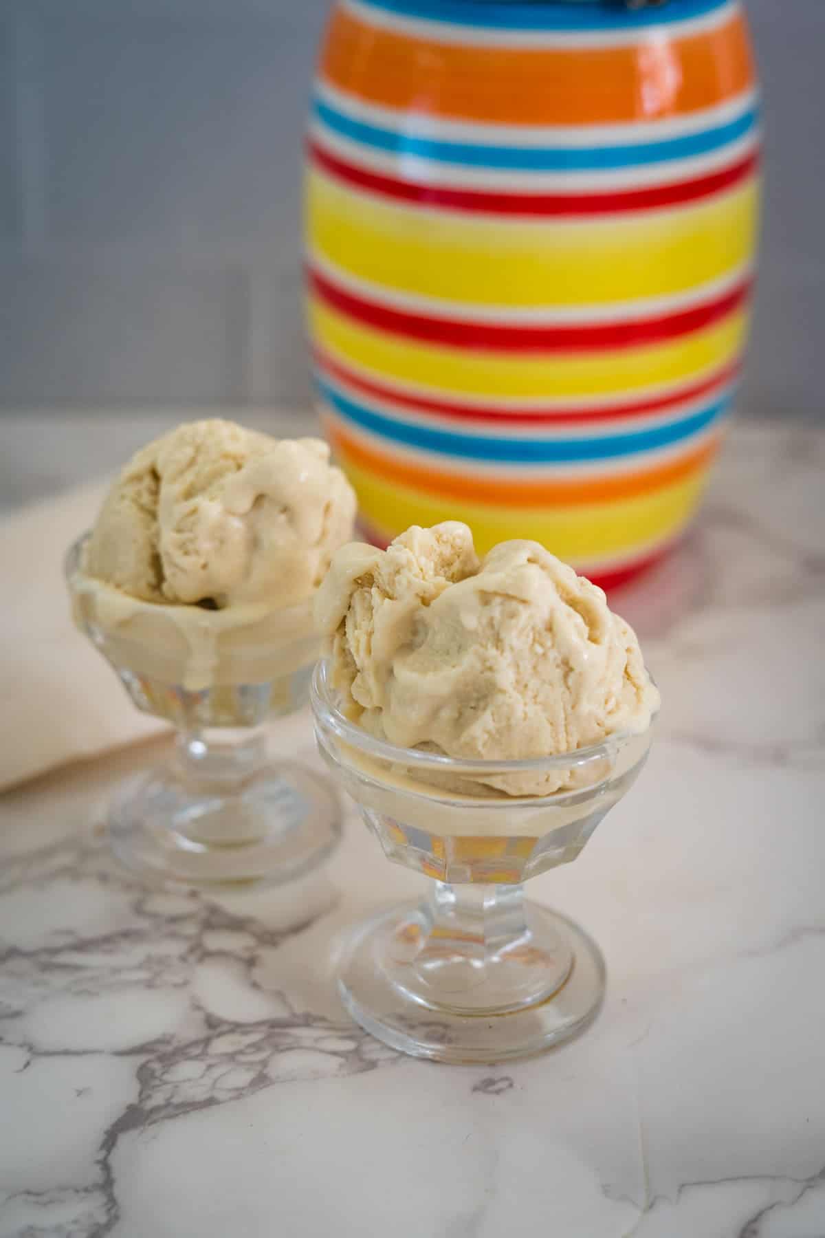 Two glass bowls of vanilla ice cream sit on a marble surface with a colorful striped vase in the background.