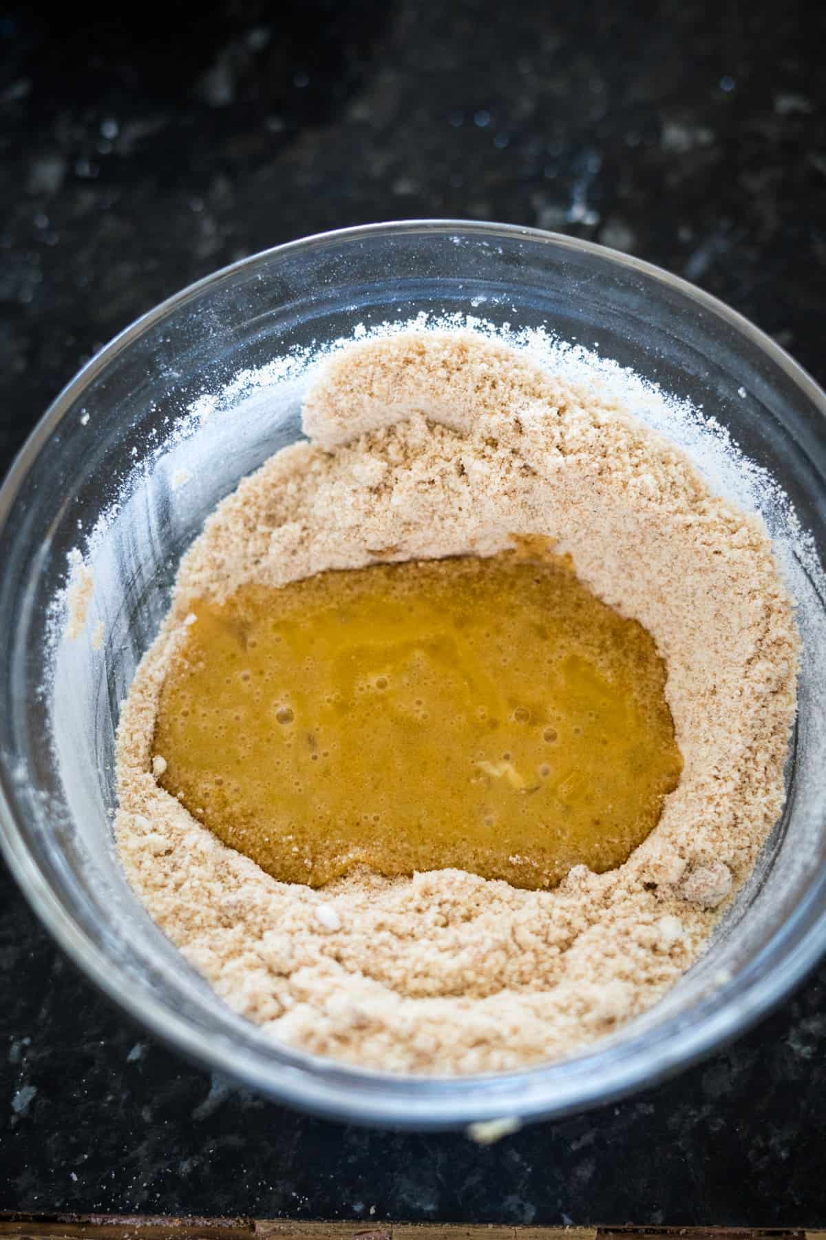 A glass bowl containing a mixture of dry ingredients with a well in the center filled with beaten eggs.