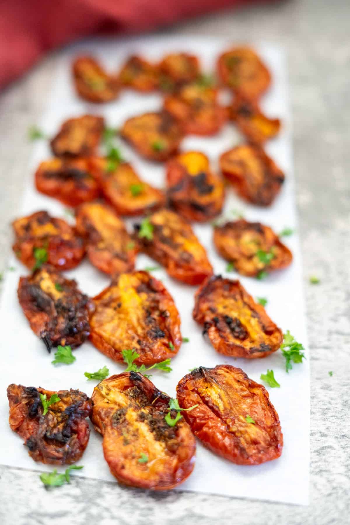 Close-up of numerous sun-dried tomato halves arranged on parchment paper, garnished with small green herbs.