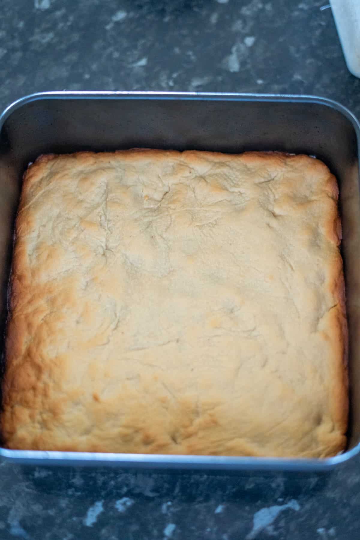 A square-shaped pan containing a baked crust with a light brown, slightly uneven surface.