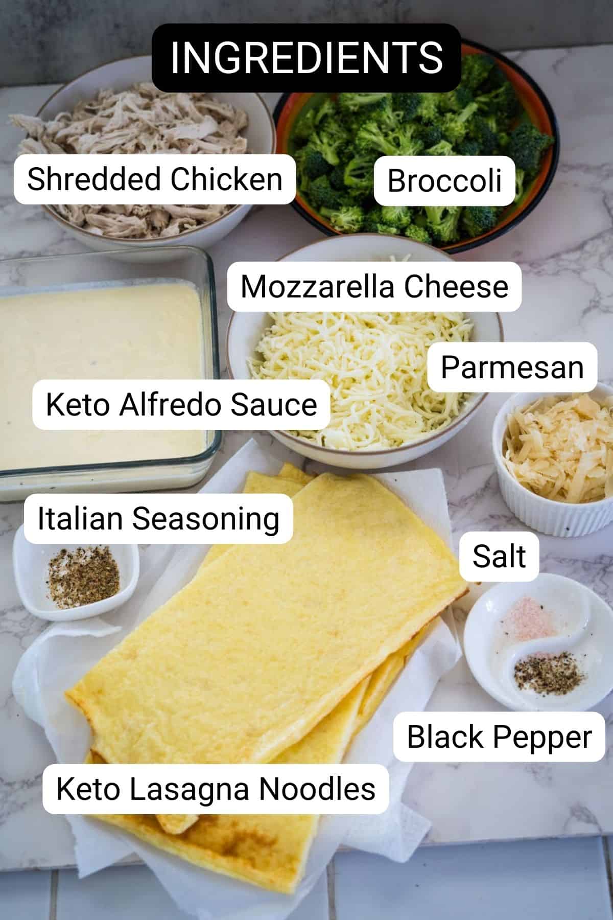 Ingredients for a delicious keto chicken broccoli lasagna laid out on a counter include shredded chicken, broccoli, mozzarella cheese, parmesan, keto Alfredo sauce, Italian seasoning, salt, black pepper, and keto lasagna noodles.