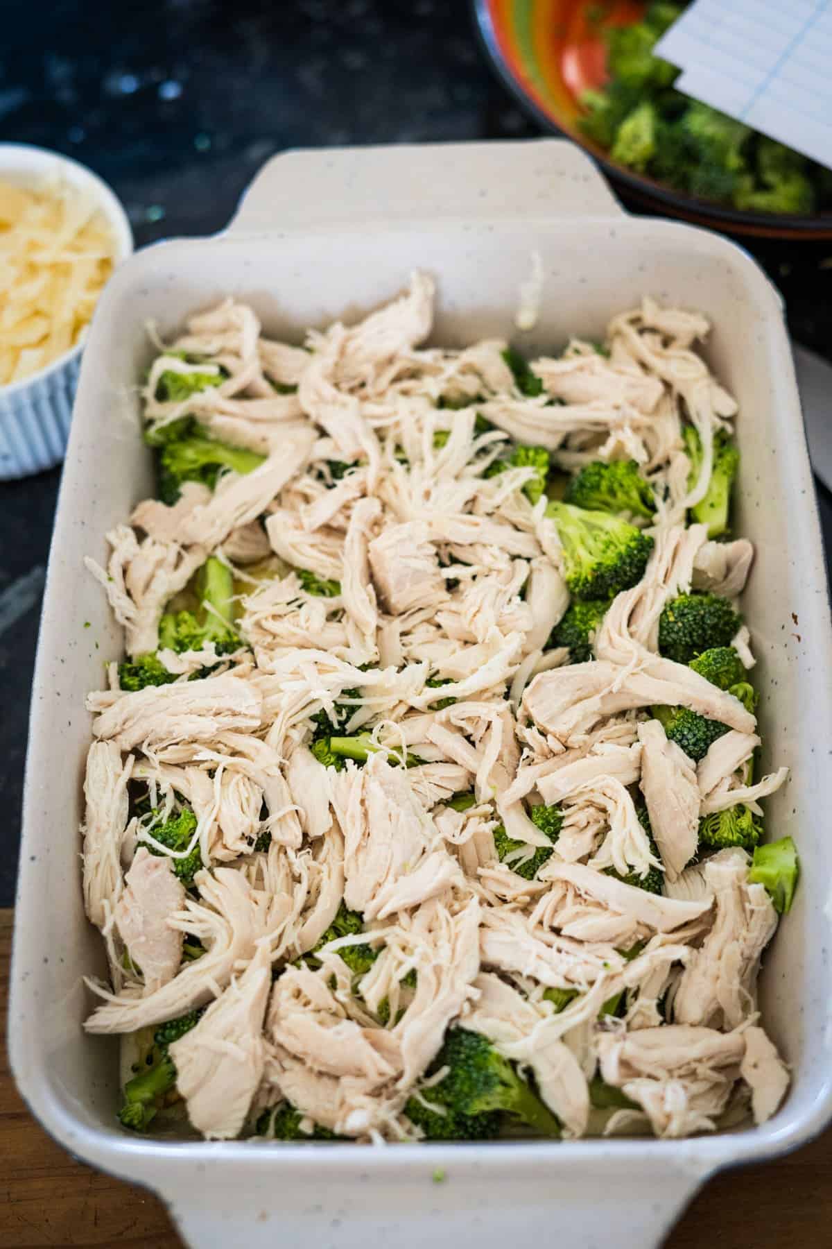 A white baking dish filled with shredded chicken and broccoli florets.