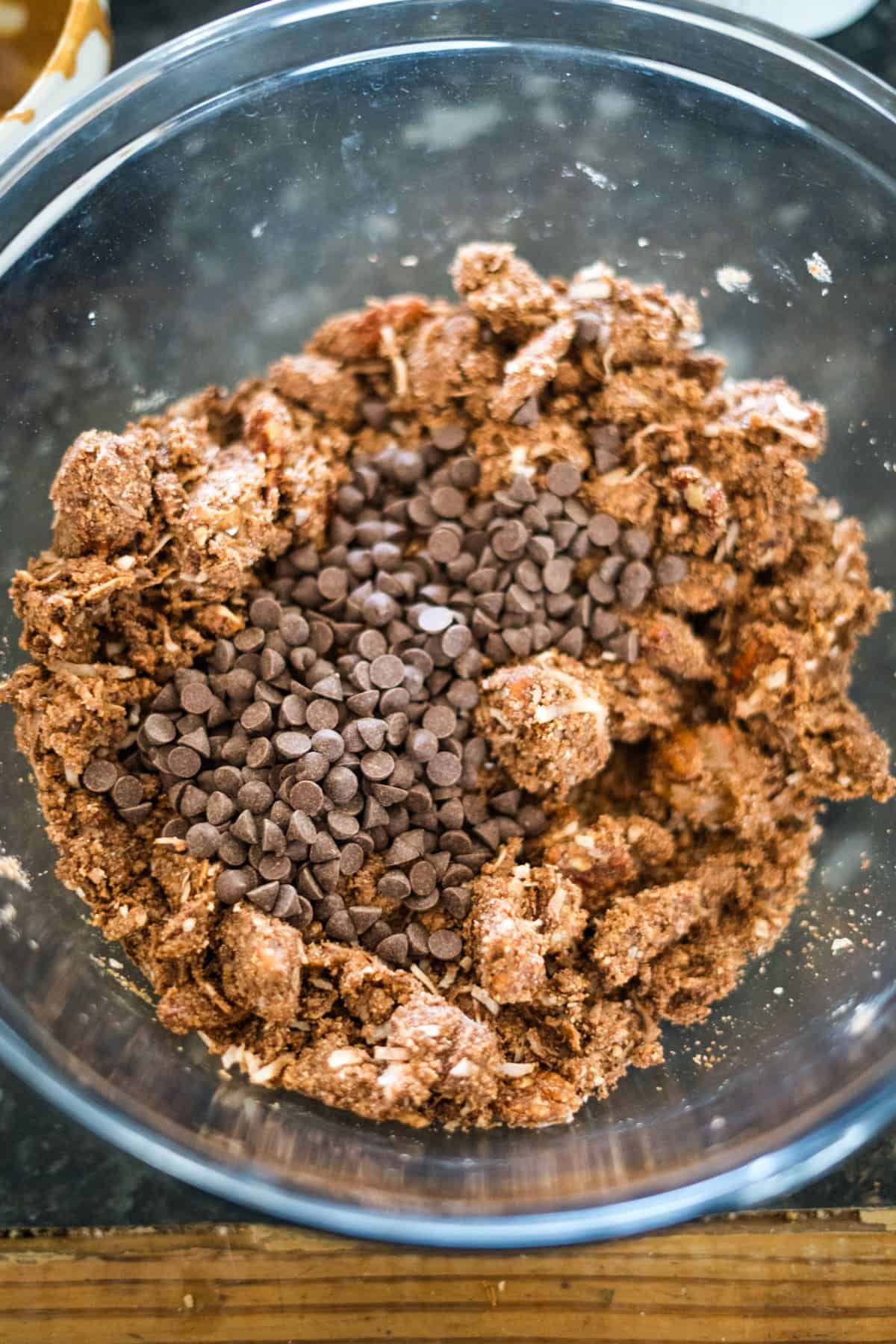 A glass bowl containing a mixture of cookie dough and chocolate chips on a dark countertop.