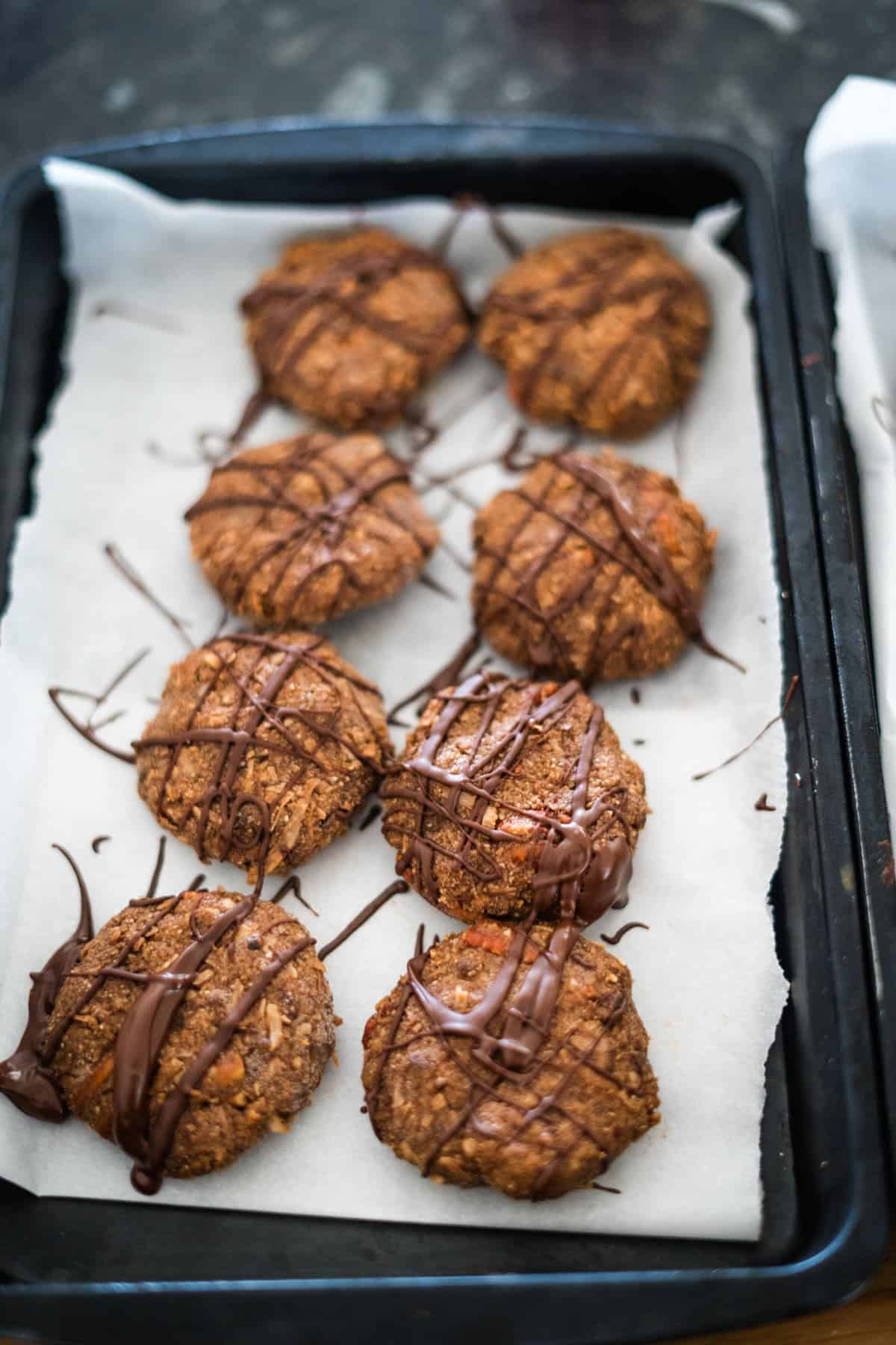 A tray of eight chocolate-drizzled cookies on parchment paper.