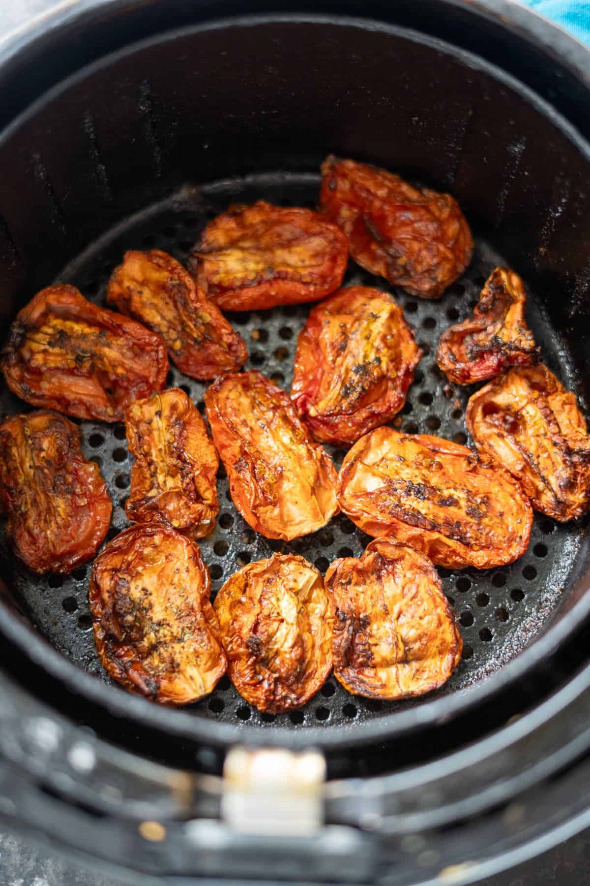 An air fryer basket filled with roasted tomato halves, showing a caramelized and slightly charred surface, reminiscent of sun-dried tomatoes.