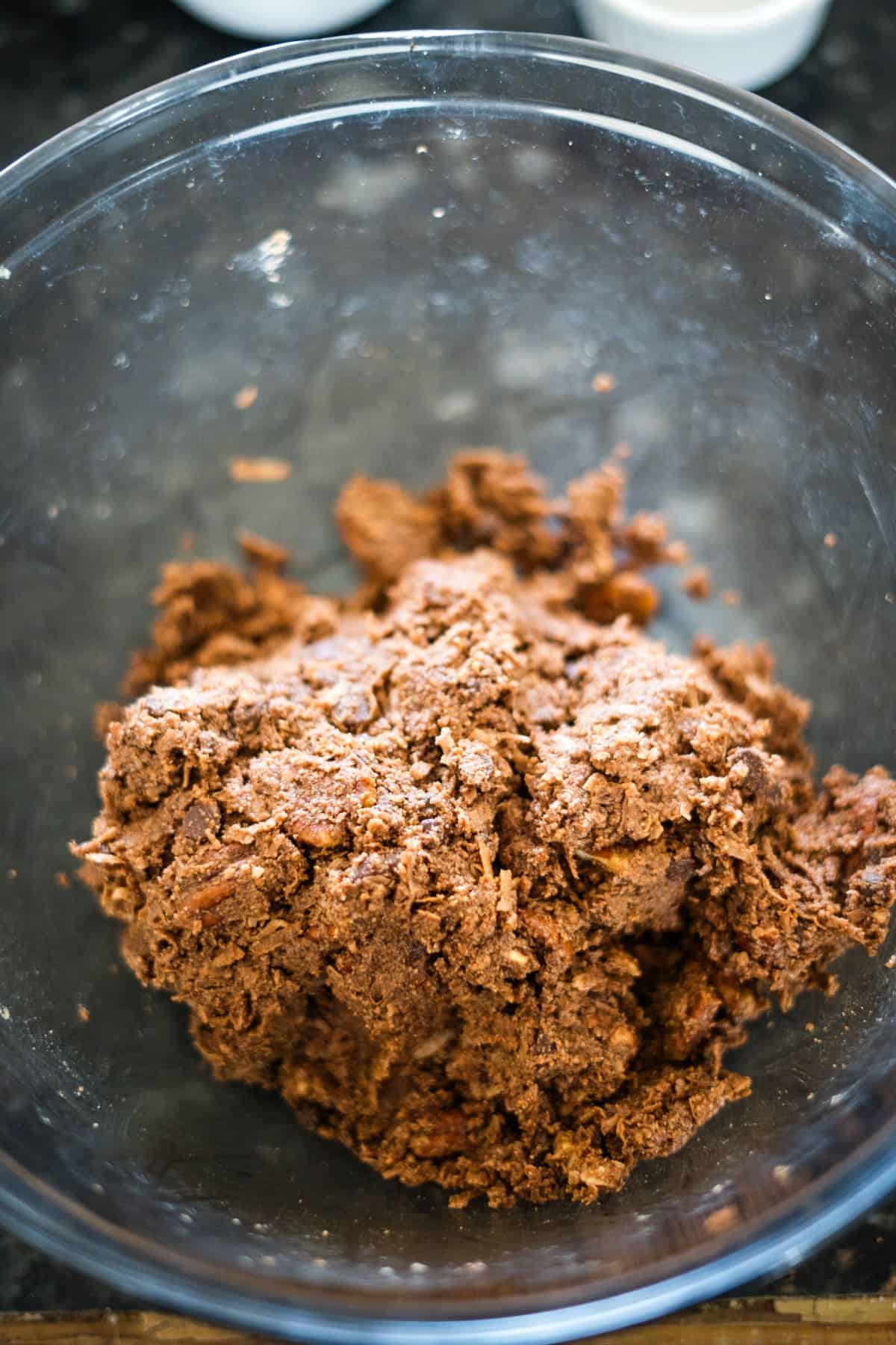 A clear bowl containing a large portion of mixed chocolate dough sits on a dark countertop.