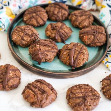 A plate and table with chocolate drizzled cookies on display, some on a blue-green plate and others on a white surface.