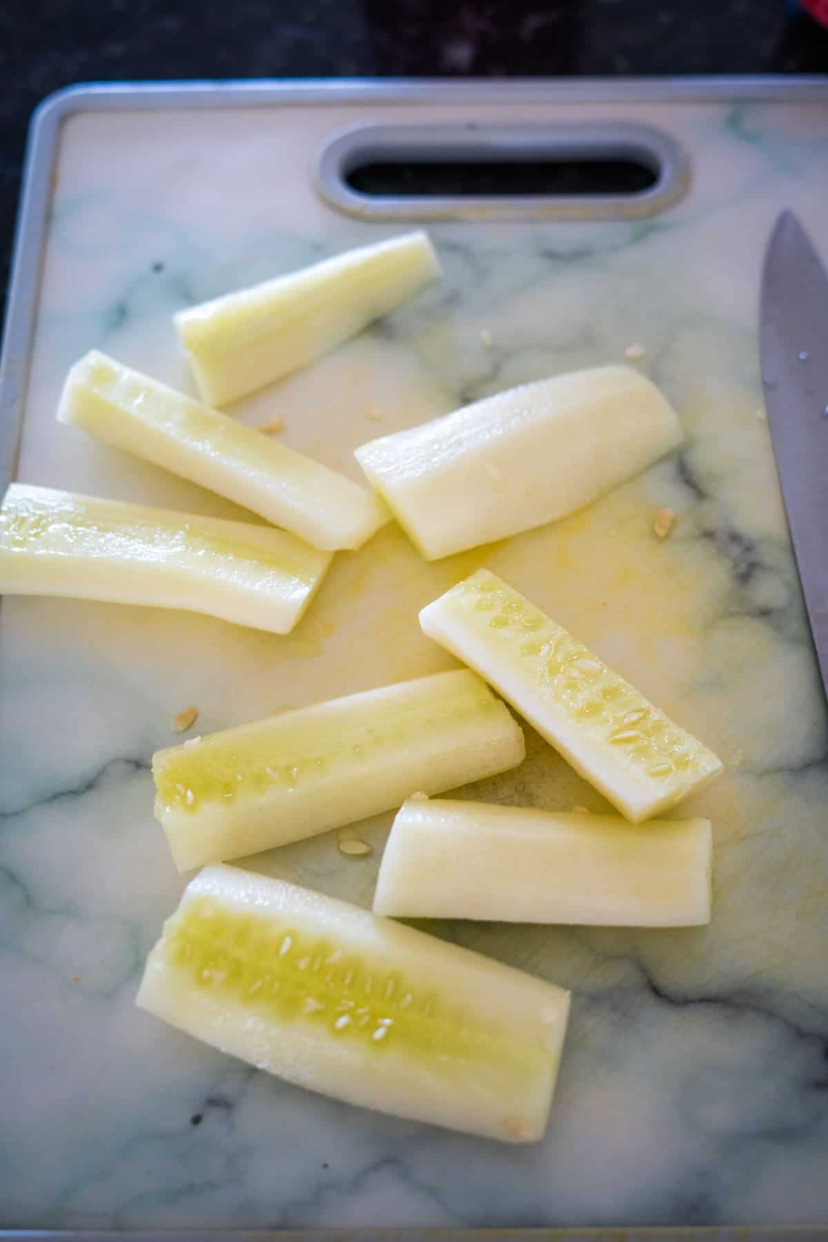 Cucumber slices arranged on a white marble cutting board with a knife beside them, perfect for pairing with a delicious cucumber cream cheese dip.