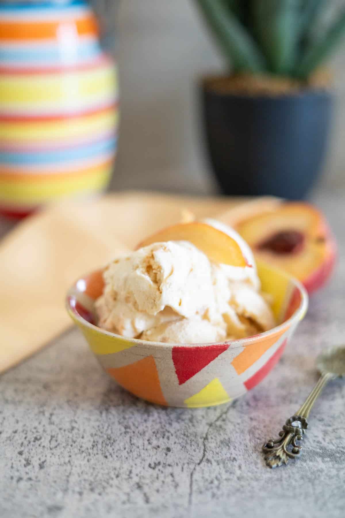 A bowl of ice cream with peach slices, next to a decorative spoon and a striped vase, on a gray countertop.