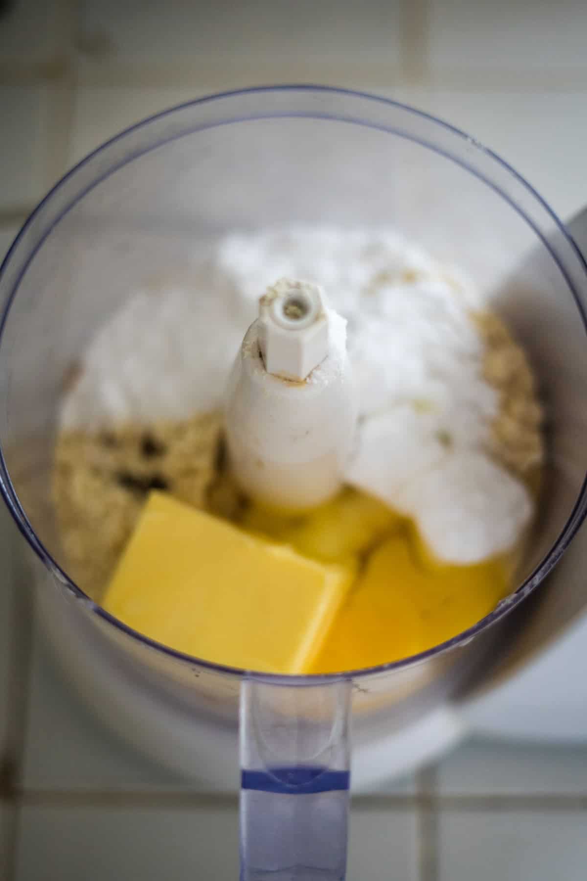 Food processor containing butter, eggs, flour, and other baking ingredients ready for mixing.