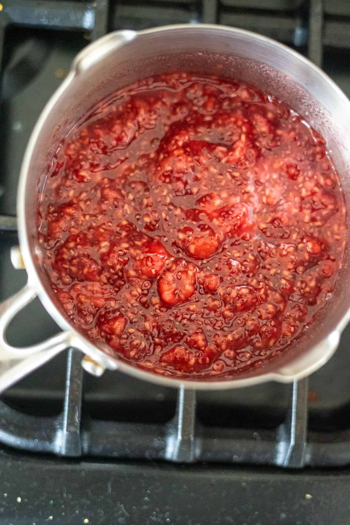 A pot of red raspberry jam cooking on a stove.