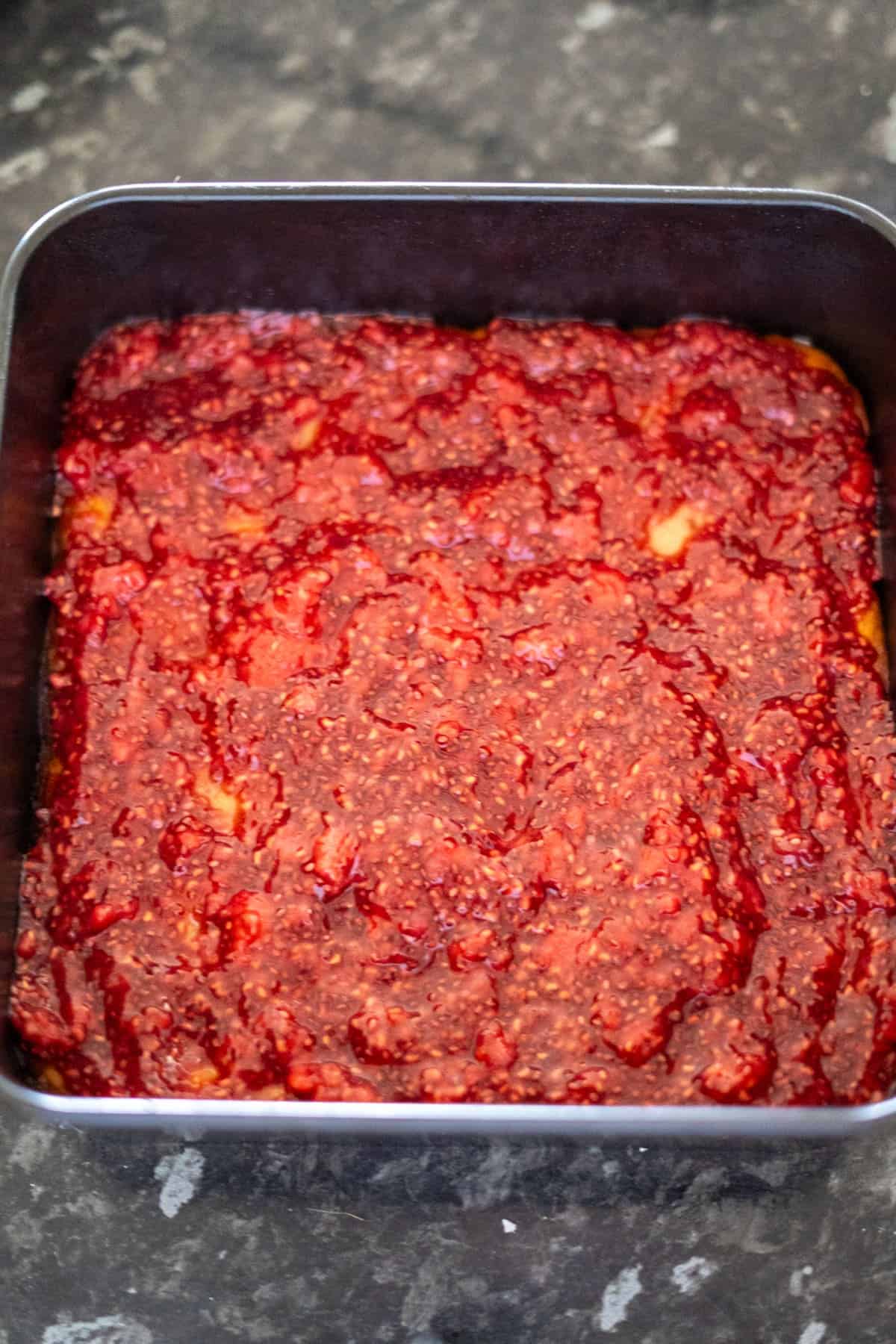 A baking pan filled with a layer of red, textured raspberry jam.