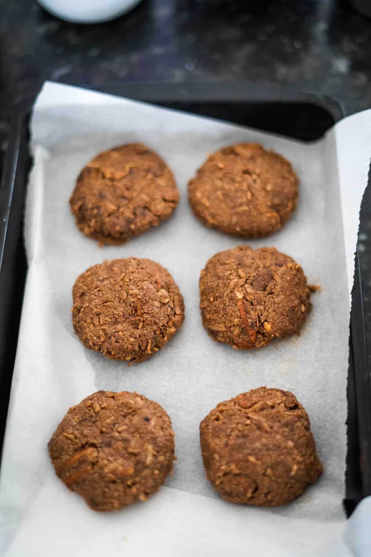 Six round, brown cookies on a parchment-lined baking tray.