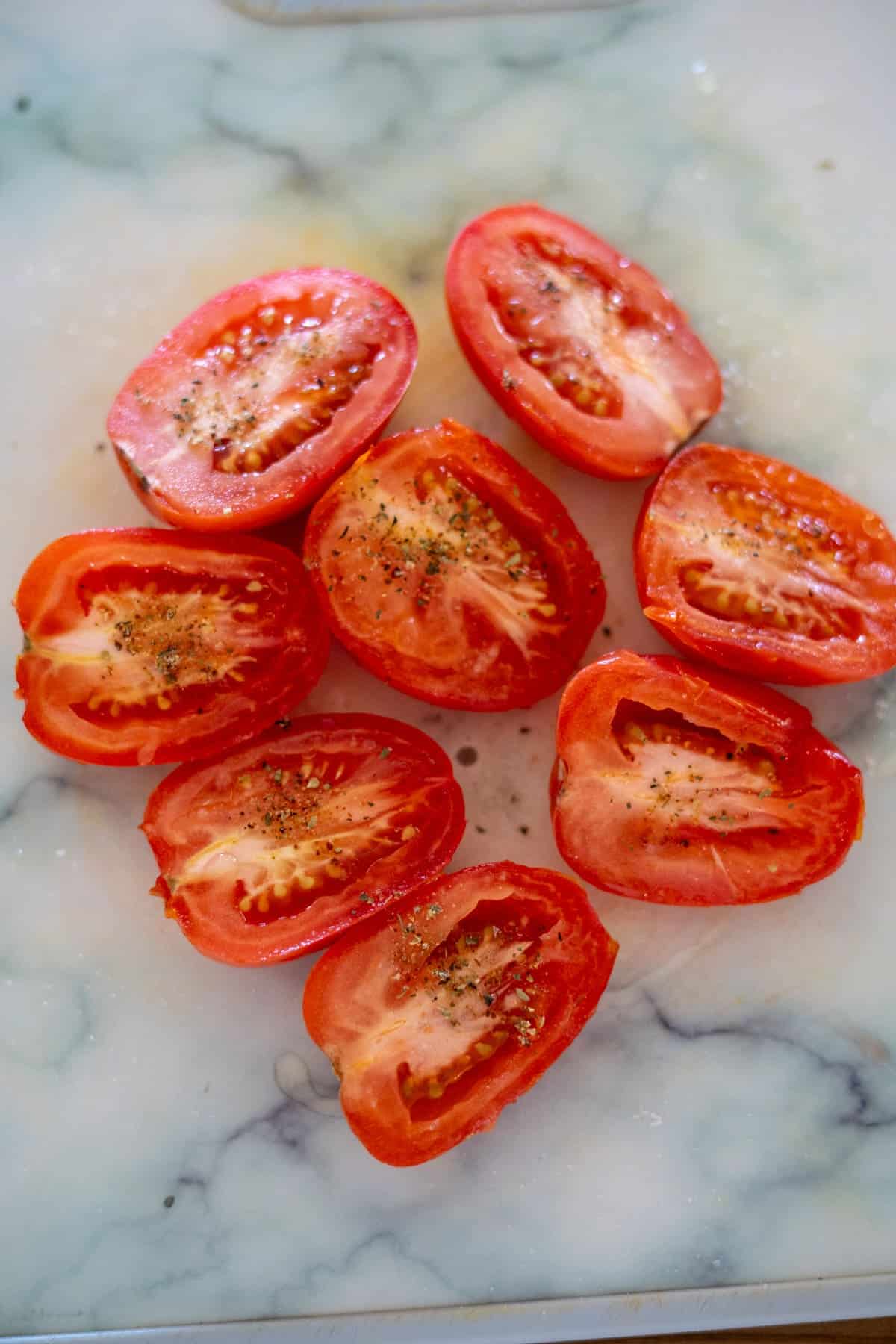 Halved tomatoes seasoned with salt and pepper are arranged on a marble surface, ready to become air fryer sun dried tomatoes.