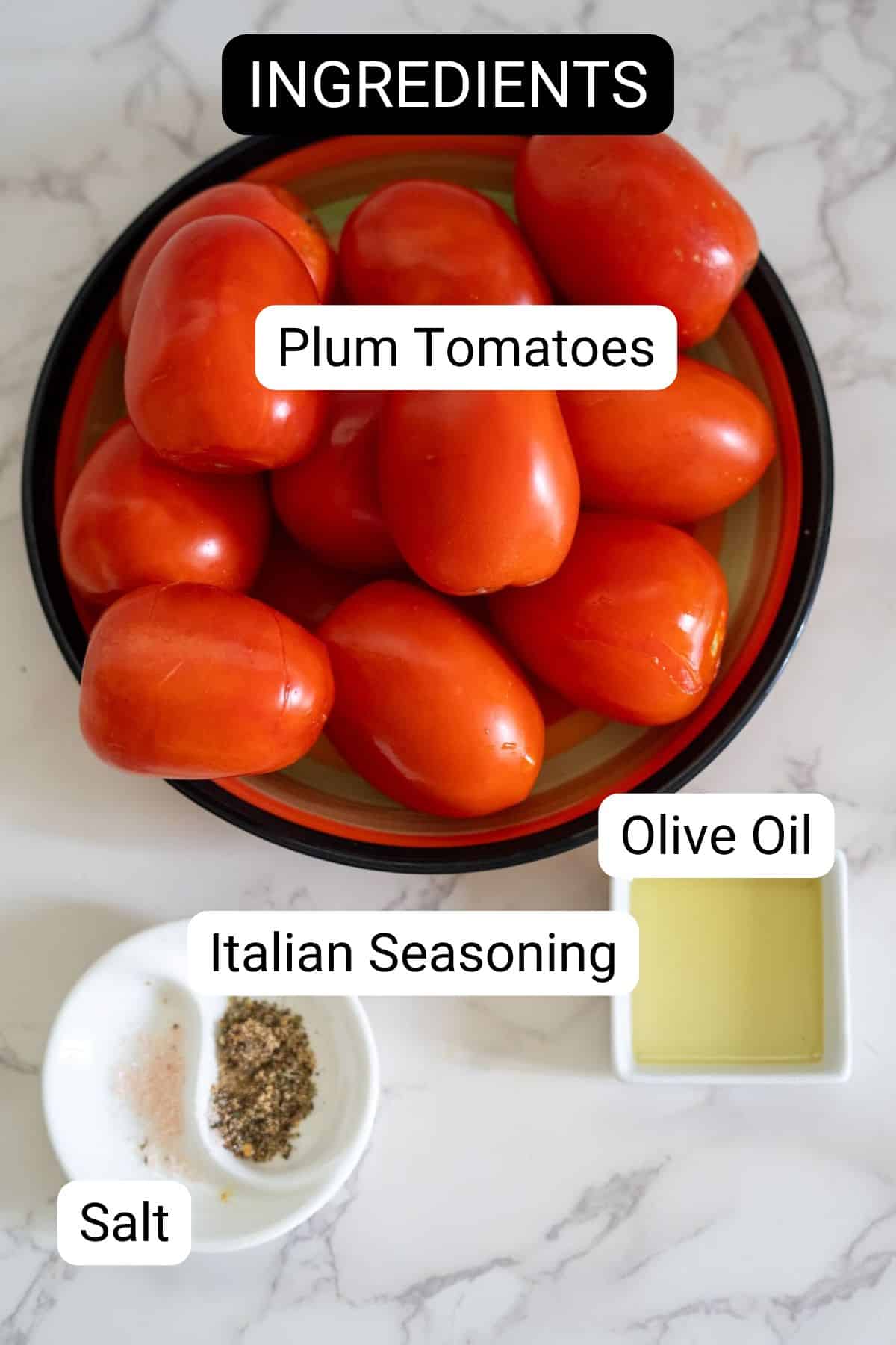 A plate of plum tomatoes, a small bowl of olive oil, a small plate with salt and pepper, and a bowl of Italian seasoning, all essentials for preparing delicious Air Fryer Sun Dried Tomatoes, are labeled as ingredients on a marble surface.