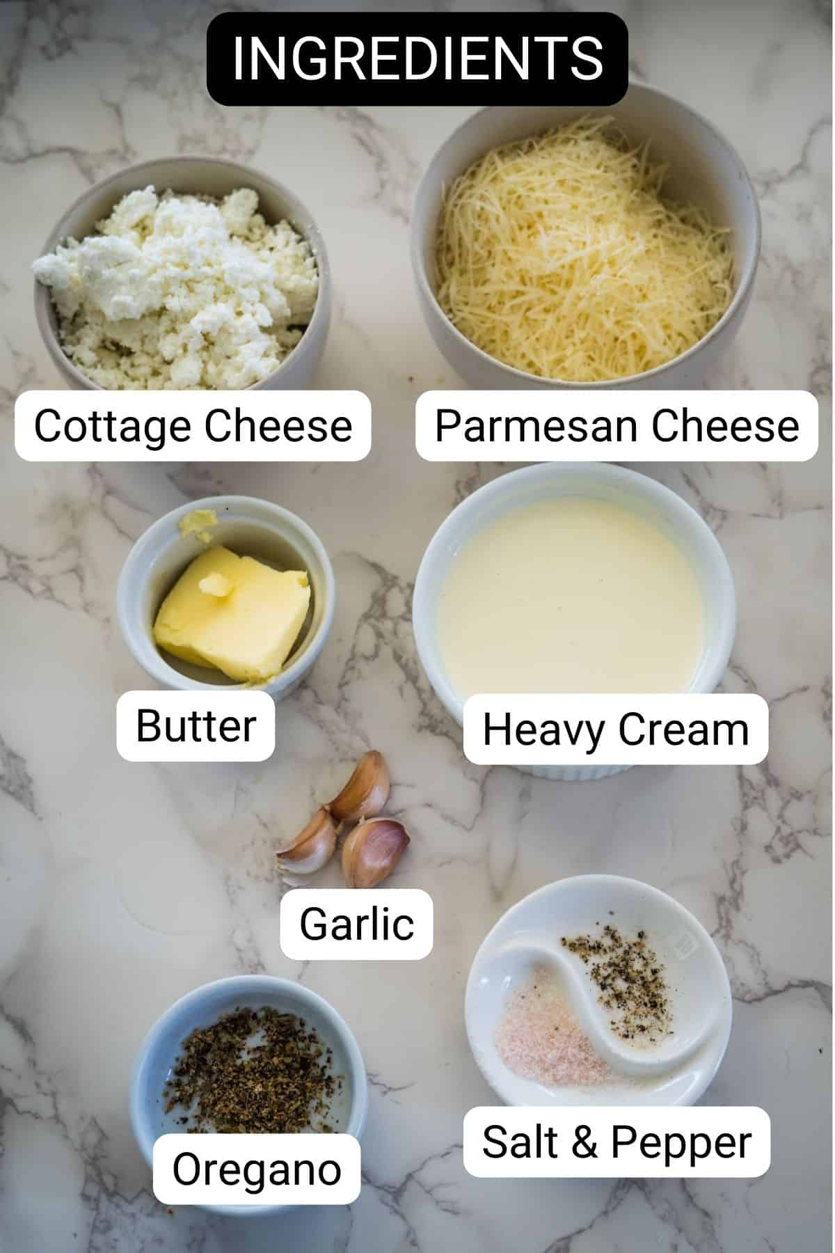 Ingredients for a dish arranged on a marble surface: cottage cheese, Parmesan cheese, butter, heavy cream, garlic cloves, oregano, and a mix of salt and pepper.