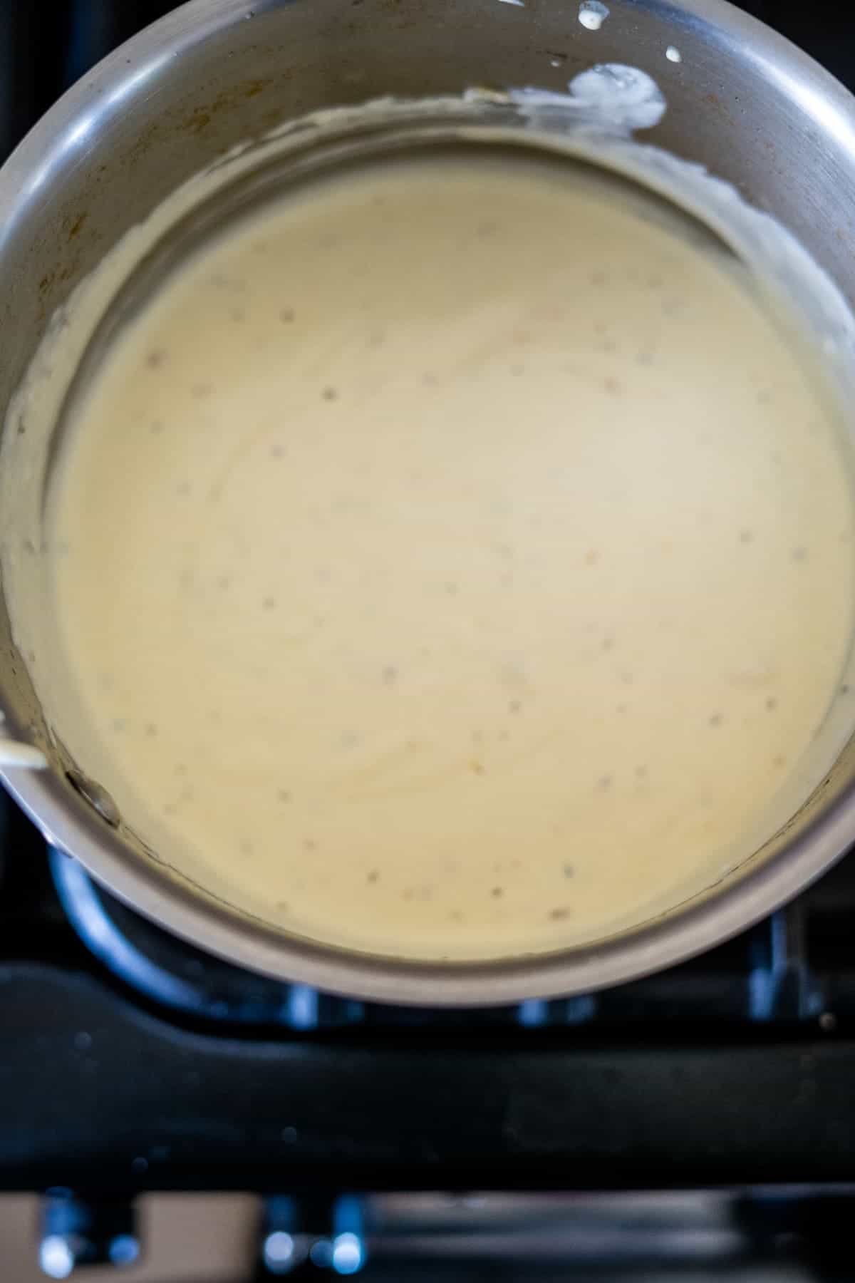 A pot filled with a smooth, light yellow sauce, cooking on a stovetop.