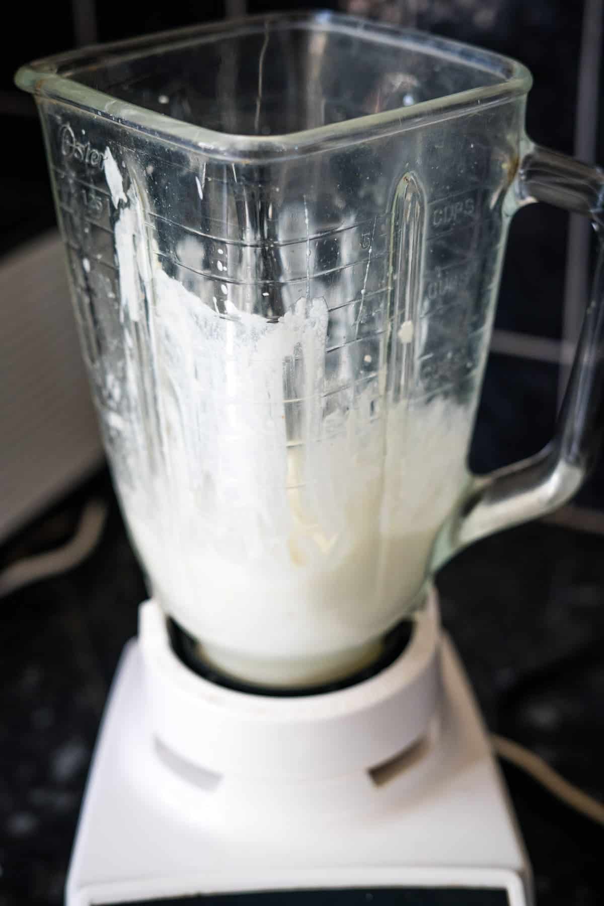 A blender filled with a partially blended white liquid is resting on a kitchen counter.