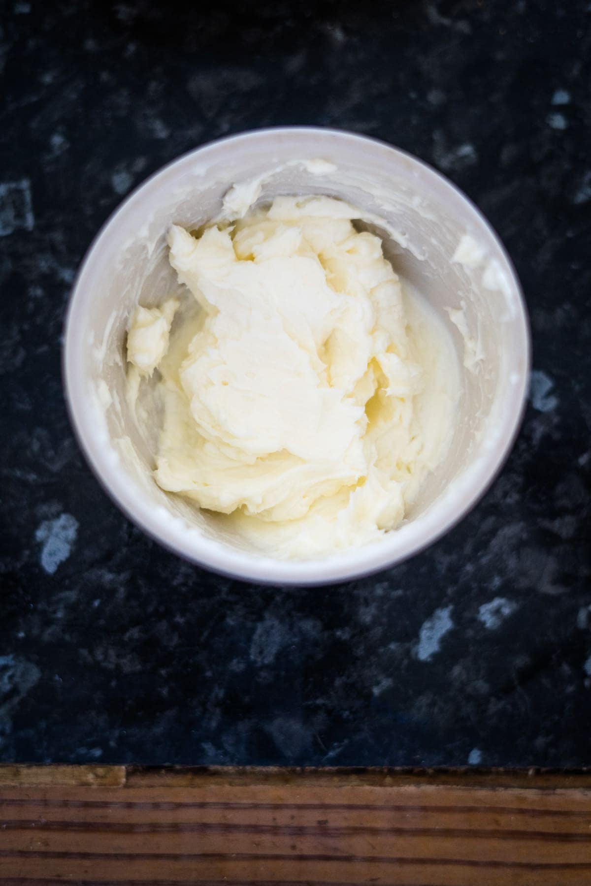 A bowl of softened butter sits on a dark marble countertop, ready to be used for making delicious keto pumpkin cheesecake muffins.