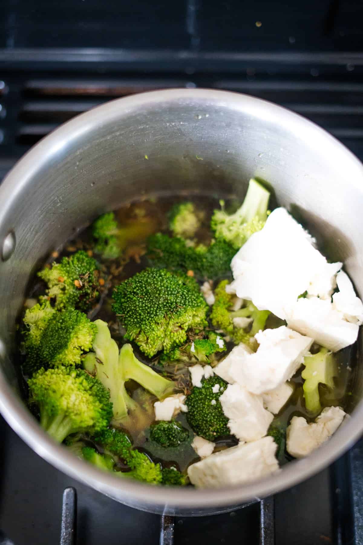 A pot on a stove contains broccoli florets and chunks of white tofu simmering in liquid.