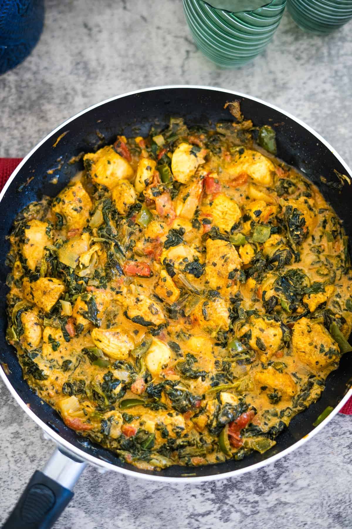 A skillet filled with a creamy dish featuring chicken pieces, spinach, tomatoes, and various herbs and spices.