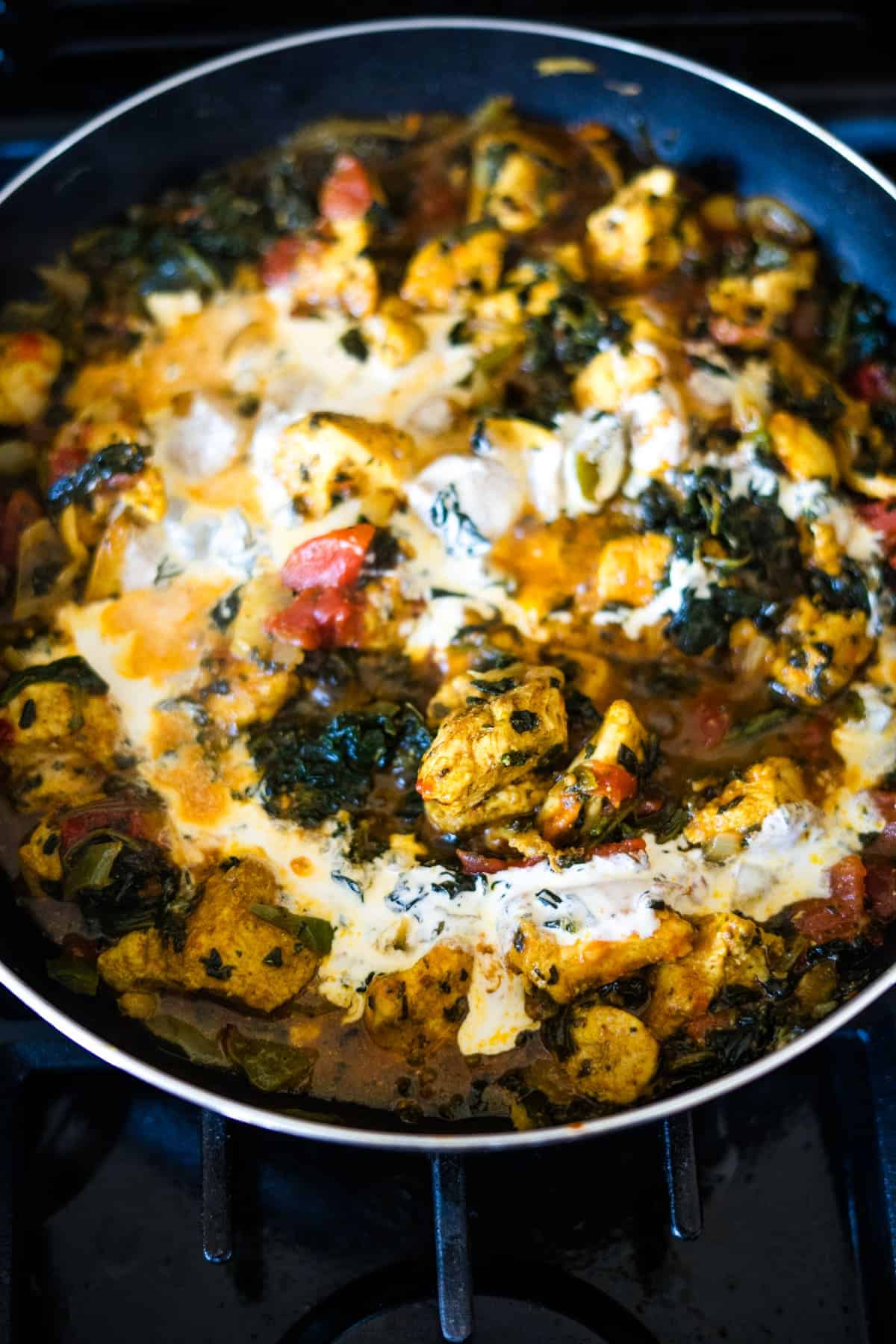 A pan filled with cooked chicken, tomatoes, spinach, and a creamy sauce on a stove.