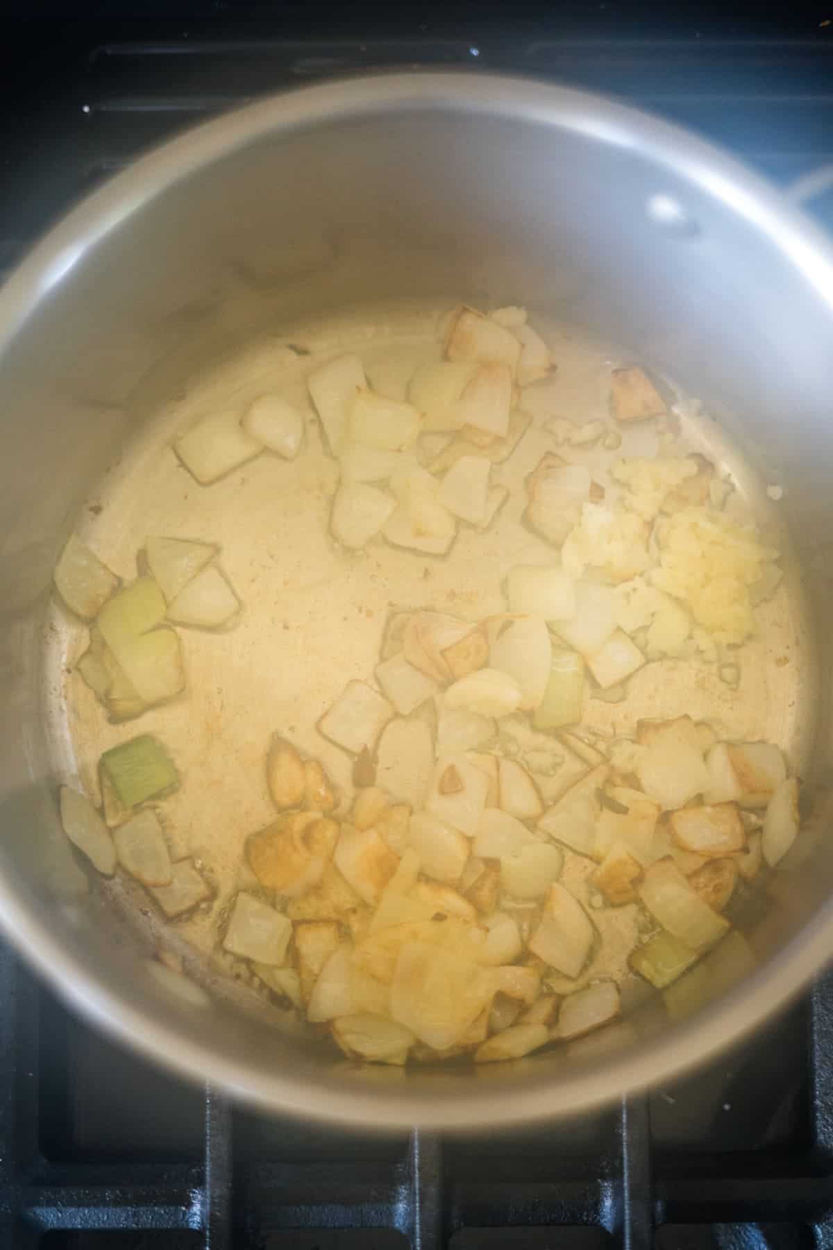 Chopped onions and garlic are being sautéed in a stainless steel pot on a stove, creating the flavorful base for a delicious keto pumpkin chili.