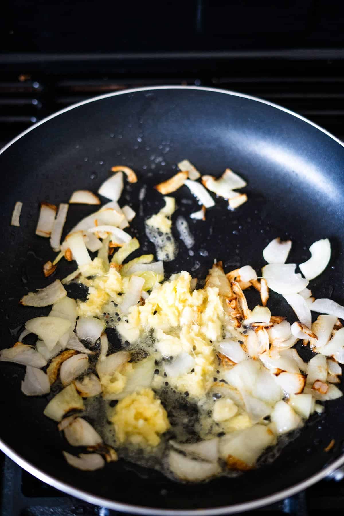 Chopped onions and minced garlic cooking in a non-stick frying pan.