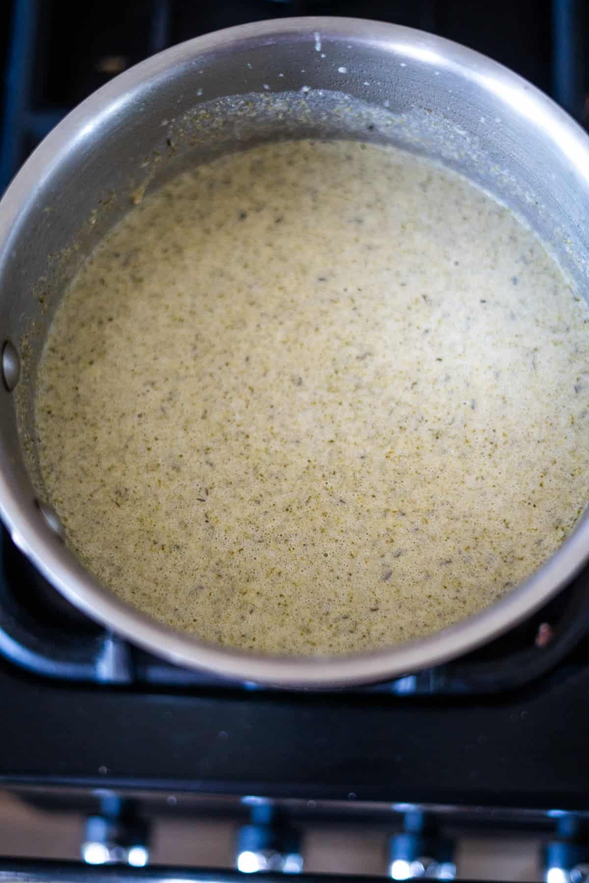 A pot of soup in the process of cooking on a stovetop, containing a light green, creamy mixture.