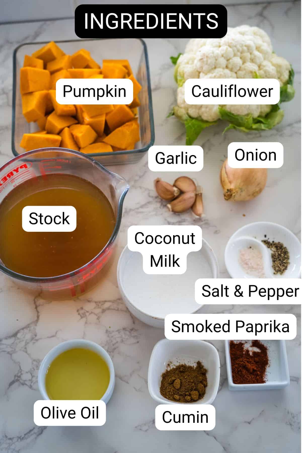 Ingredients for cooking a delicious pumpkin cauliflower soup: pumpkin, cauliflower, garlic, onion, stock, coconut milk, olive oil, salt & pepper, smoked paprika, and cumin—all elegantly arranged on a marble countertop.