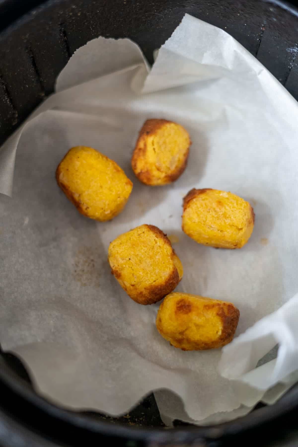 Five golden-brown potato cubes on parchment paper inside an air fryer.