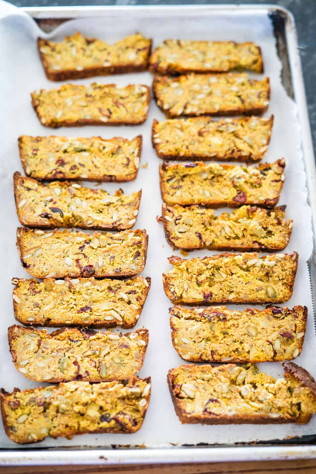 A baking tray with sixteen slices of nut and seed loaf arranged in neat rows on parchment paper.