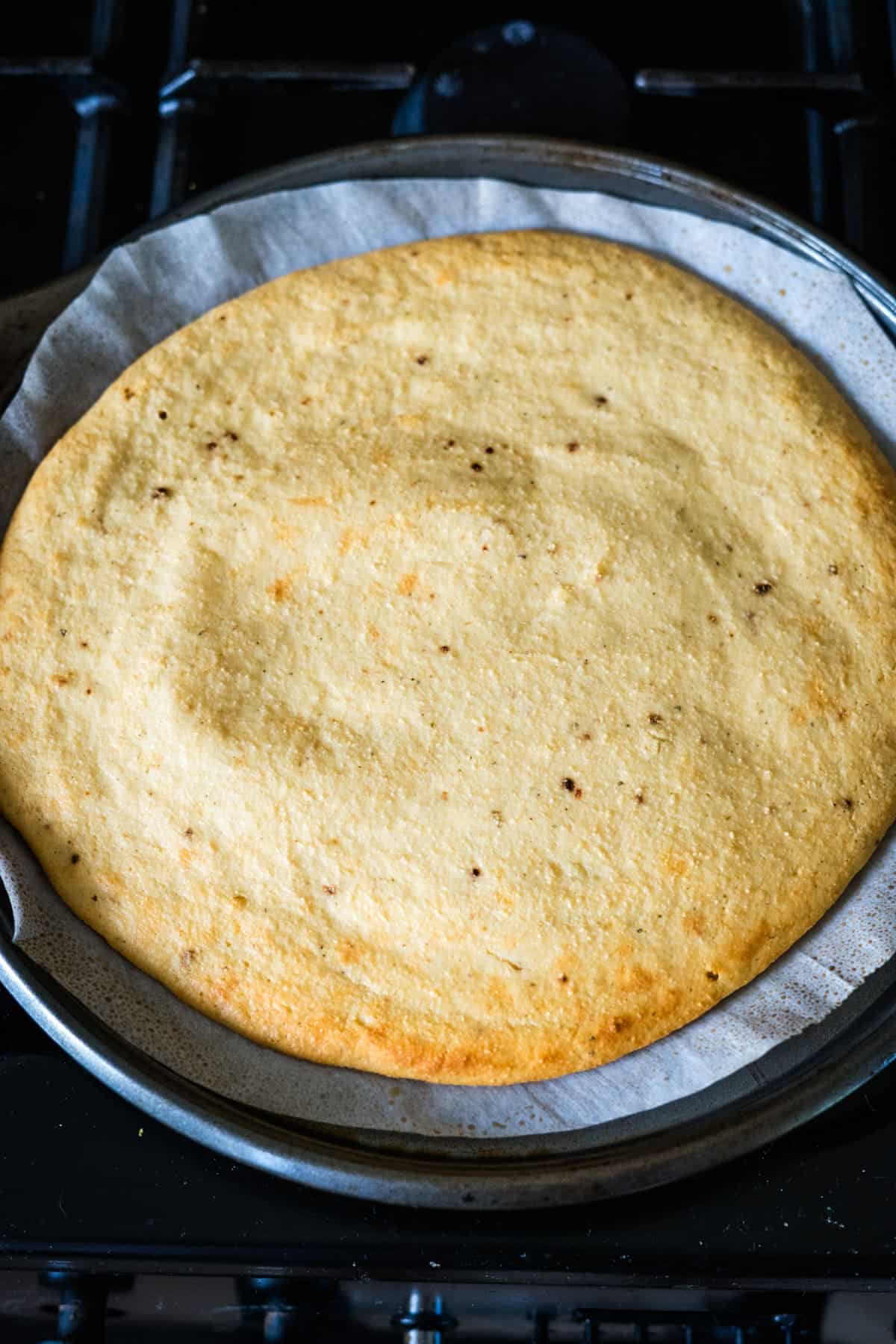 A round vanilla sponge cake on a baking tray lined with parchment paper.