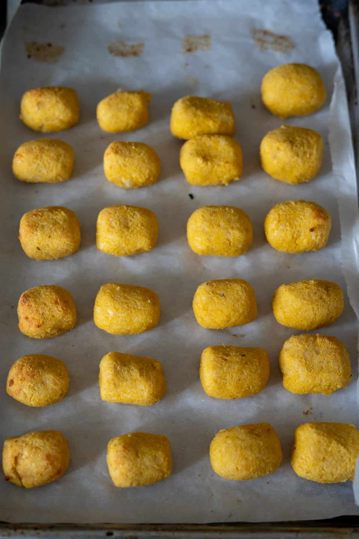 Rows of yellow croquettes on a parchment-lined baking sheet.