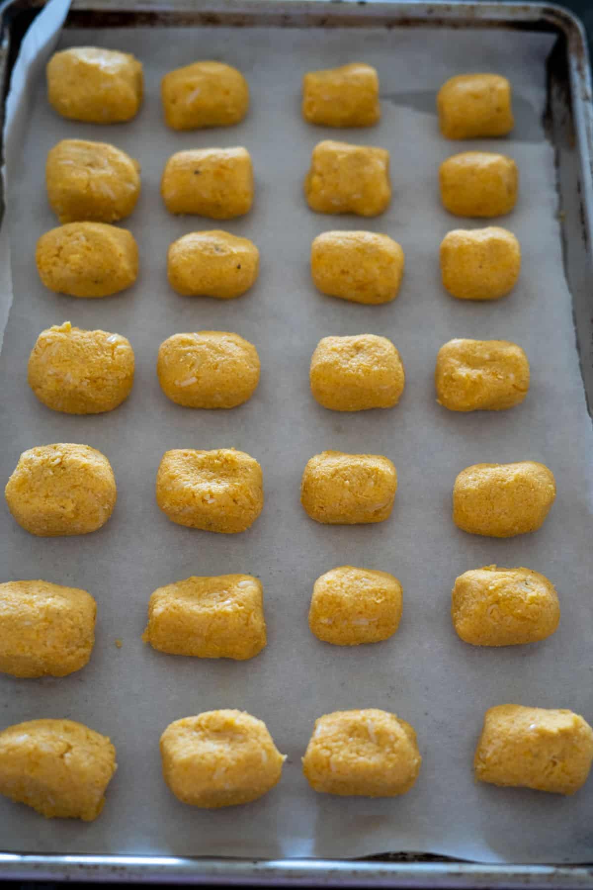 Rows of uncooked orange dough pieces arranged on a parchment-lined baking tray.