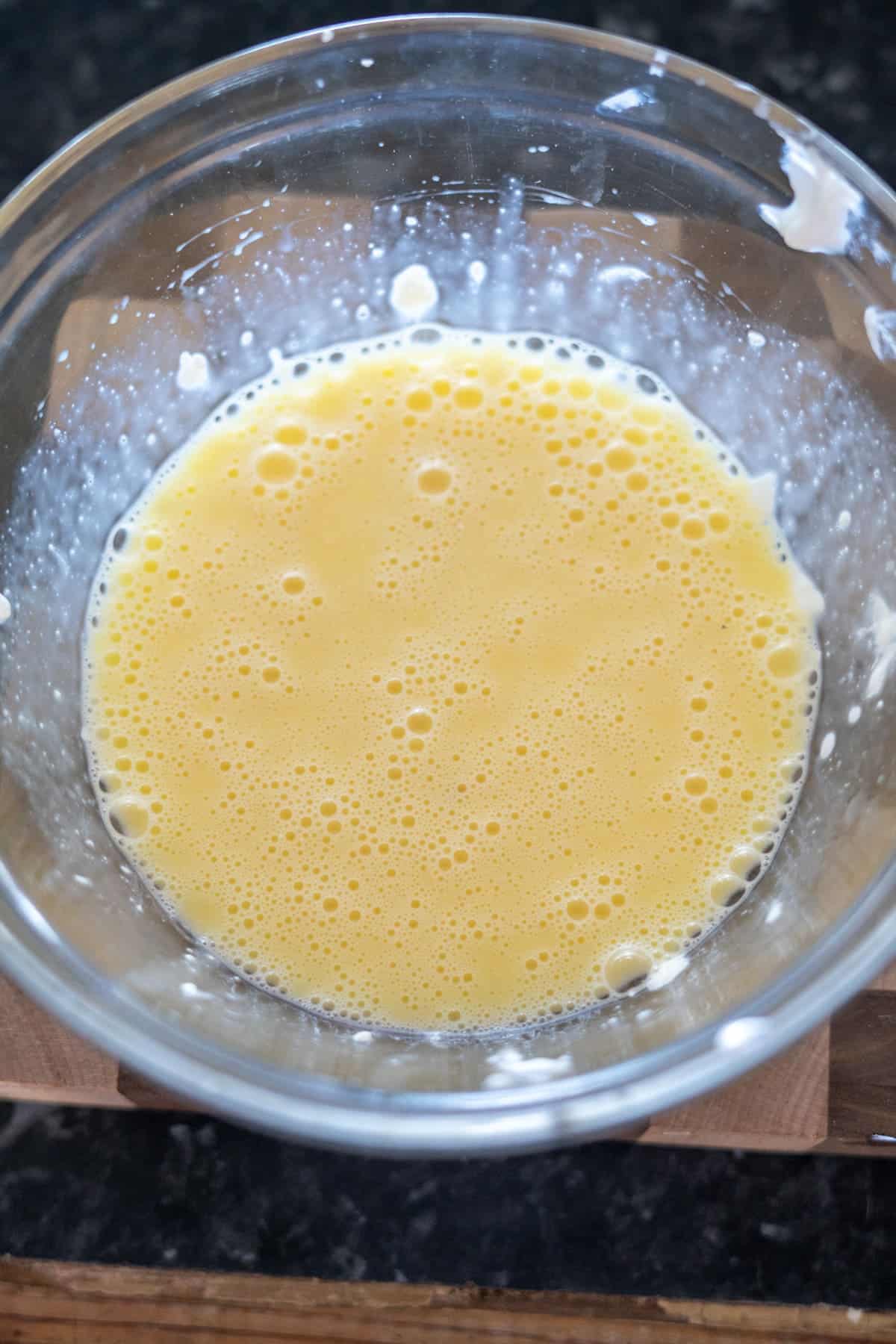 A glass bowl filled with beaten eggs on a wooden surface.