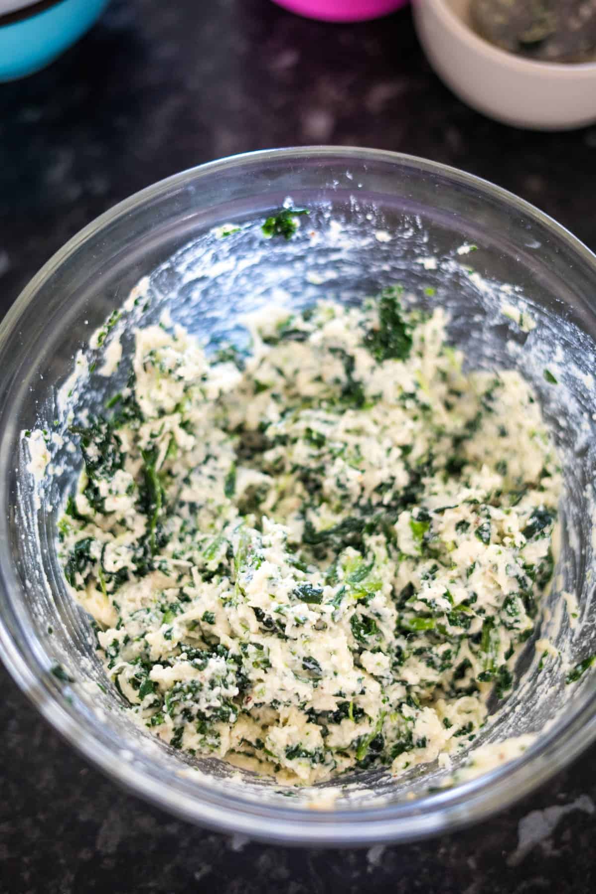 A bowl of spinach and cheese mixture, perfect for creating a keto spinach lasagna, sits on a black countertop.