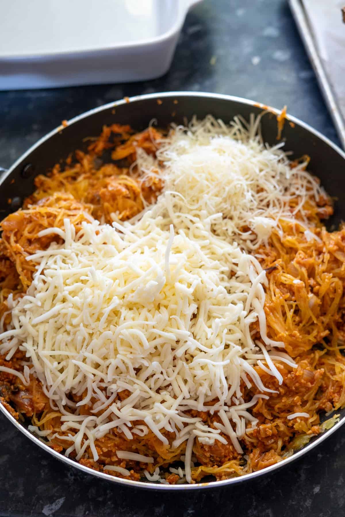 A pan filled with shredded cheese on top of cooked shredded sweet potato, placed on a dark countertop.