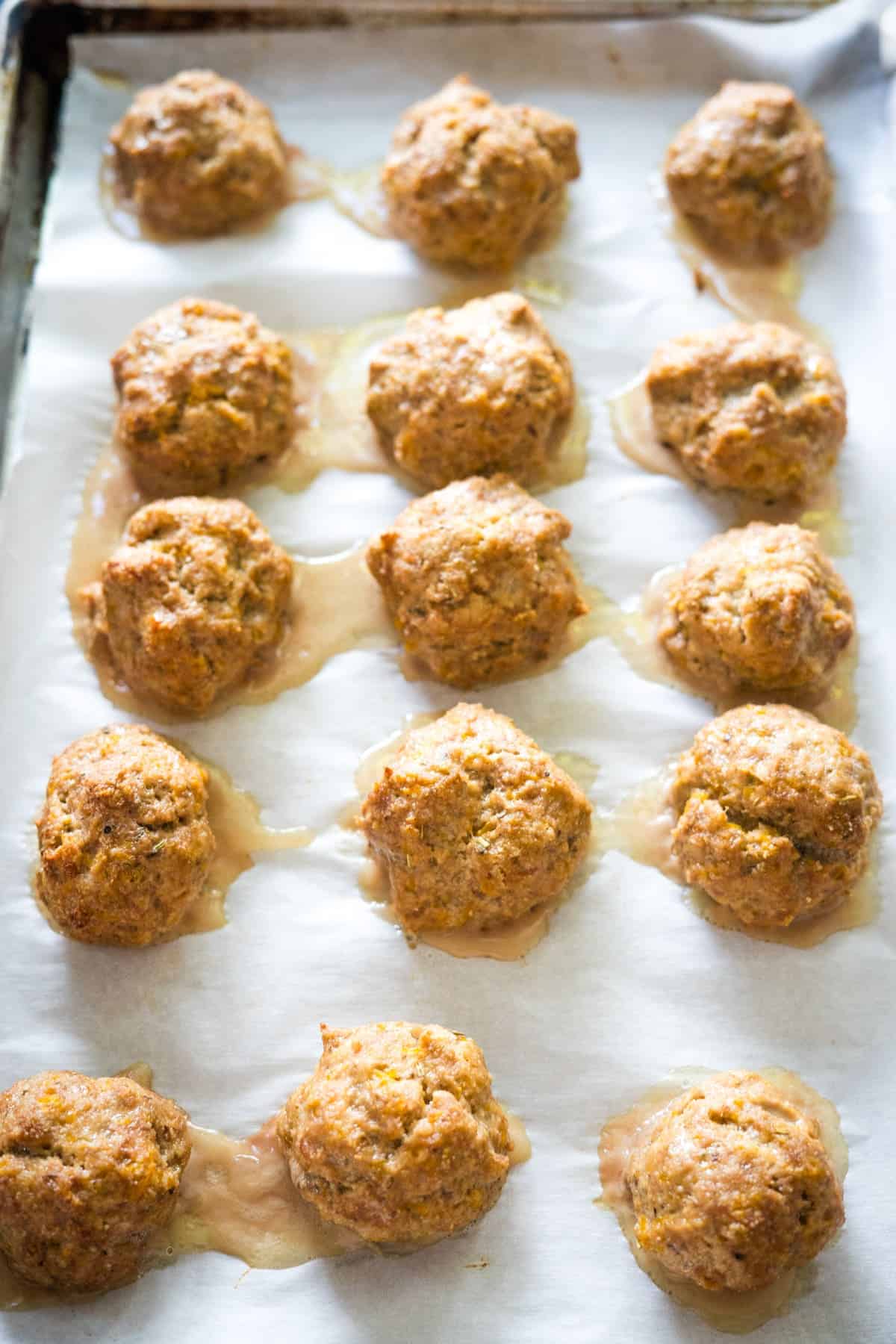 A baking sheet with parchment paper holds 15 baked sausage balls, spaced evenly in rows.